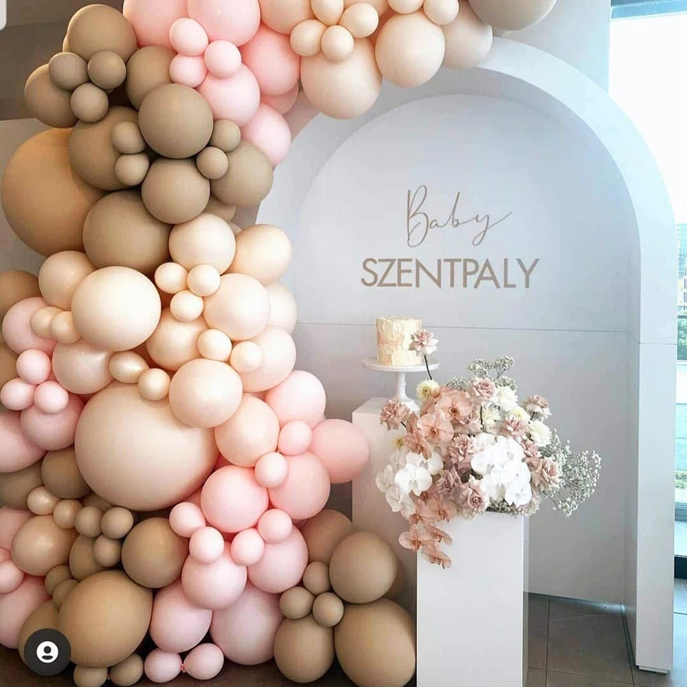 A large arrangement of assorted pink and beige latex balloons forming an archway backdrop for a baby celebration.