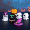 A collection of white and purple resin craft miniatures depicting ghosts and a pumpkin on a dark surface.