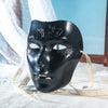 A black face mask with intricate, textured details is displayed on white fabric.