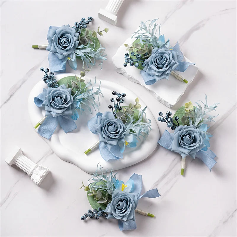 A set of six dusty blue silk rose boutonnières featuring delicate greenery and small blue filler flowers on white marble.