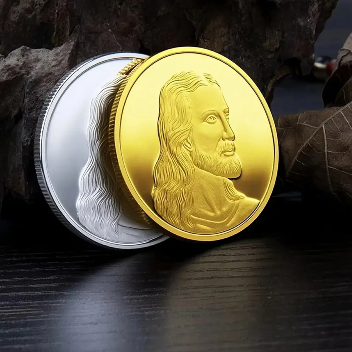A gold commemorative coin featuring a profile of Jesus Christ, resting on a dark wooden surface next to a piece of bark.