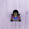 An enamel pin badge featuring a cartoon character with black hair, yellow skin, and glasses, wearing a blue shirt.