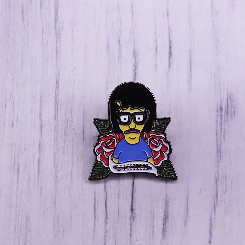 An enamel pin badge featuring a cartoon character with black hair, yellow skin, and glasses, wearing a blue shirt.