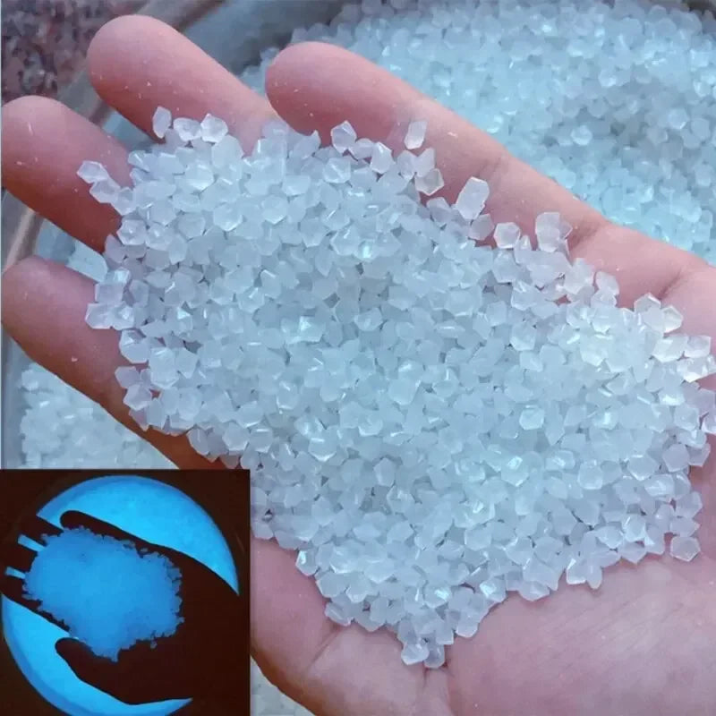 A hand holds a pile of luminous, glow-in-the-dark white pebbles for garden and aquarium decor.