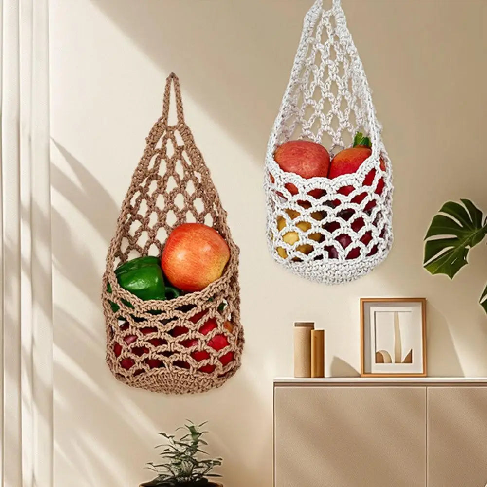 A macrame hanging storage basket filled with fresh fruits and vegetables on a light-colored wall.