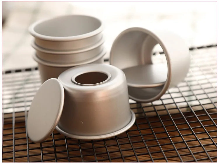 A set of five light gray non-stick round cake molds with removable bases resting on a wire rack.