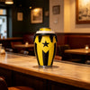 A yellow and black drum-style can holder sits on a wooden bar counter in a dimly lit restaurant setting.
