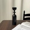 A set of two black, vintage wooden candle holders or candlesticks standing on a dark wooden table.