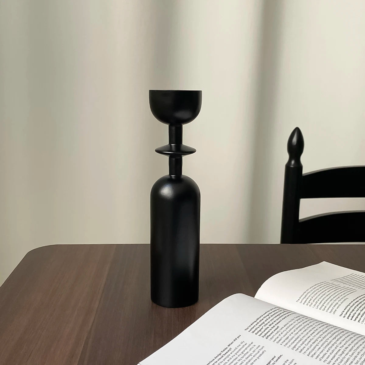 A set of two black, vintage wooden candle holders or candlesticks standing on a dark wooden table.