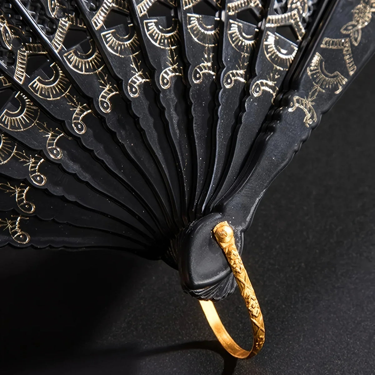 Close-up of a black folding fan decorated with gold lace patterns.