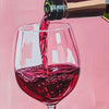 A close-up painting of red wine being poured from a bottle into a glass against a pink background.