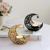 A golden crescent moon candle holder with a star charm rests on a white surface next to a book.