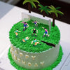 A green birthday cake decorated with soccer player toppers and field elements.