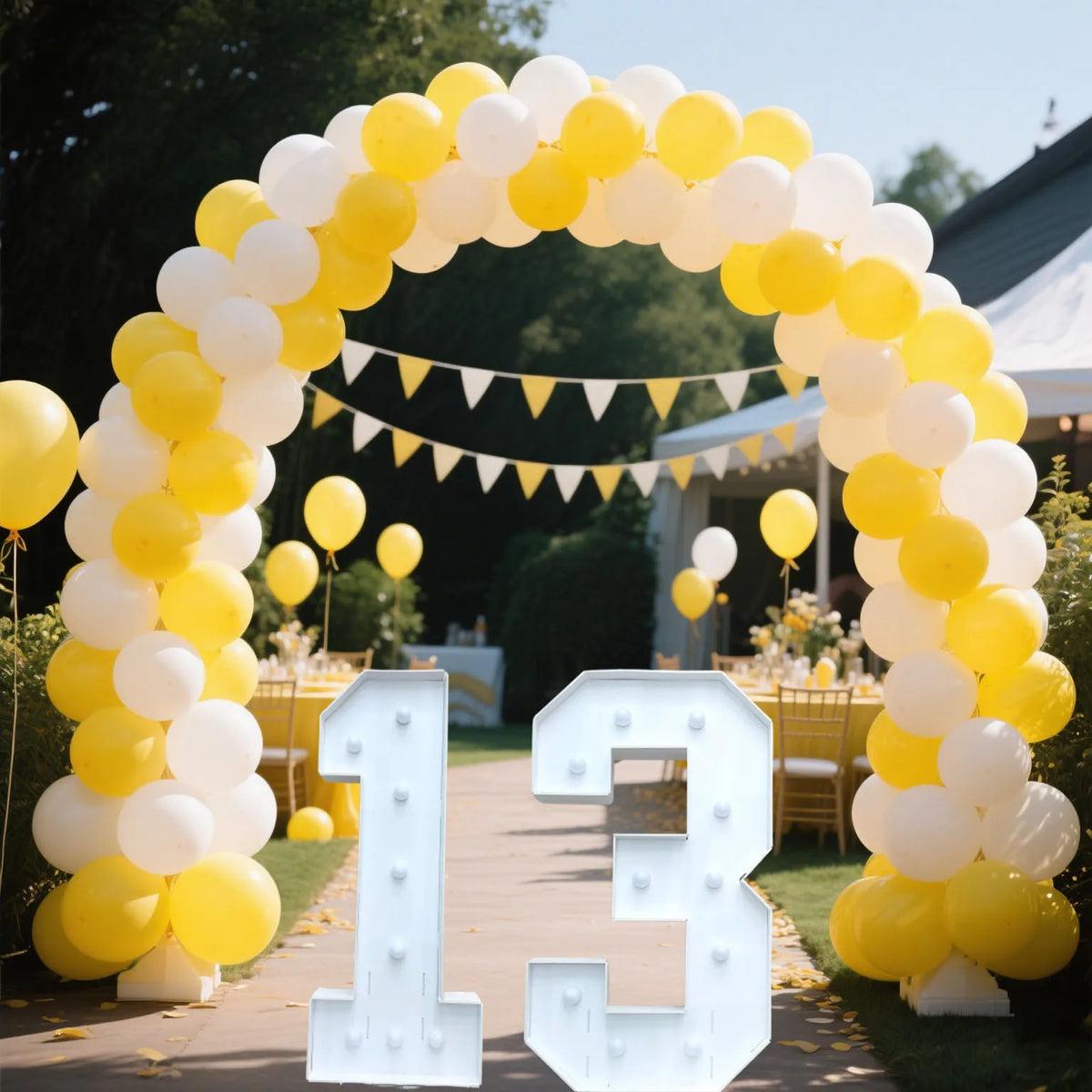A yellow and white balloon arch decorated with a light-up marquee number sign for 13.
