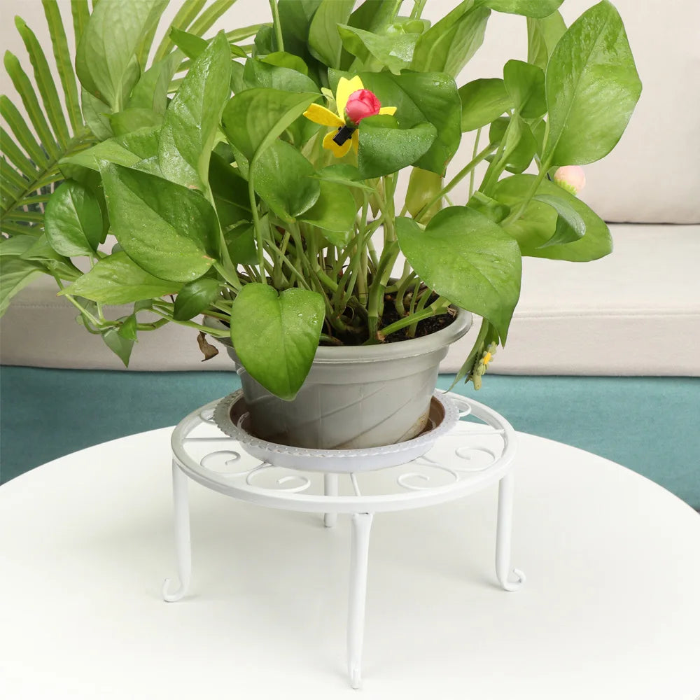 A potted green plant with yellow and pink flowers sits on a white decorative metal stand.