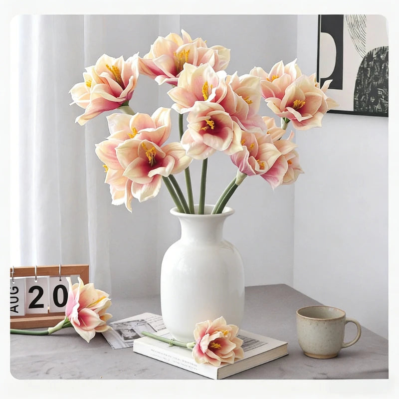 A bouquet of peach and cream artificial clivia amaryllis flowers in a white vase on a gray surface.