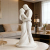 A white minimalist sculpture of a couple embracing, displayed on a table.