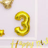 Gold foil number balloon shaped like the number three decorating a white frame for a birthday celebration