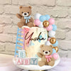 A tiered cake decorated with teddy bears and pastel balloons for a gender reveal party.