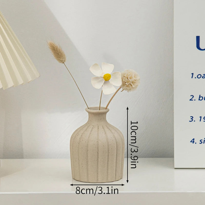 A minimalist ceramic vase with a textured finish holds dried floral elements on a white surface.