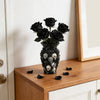 A black gothic skull resin decorative vase filled with dark roses and scattered skulls on a wooden surface.