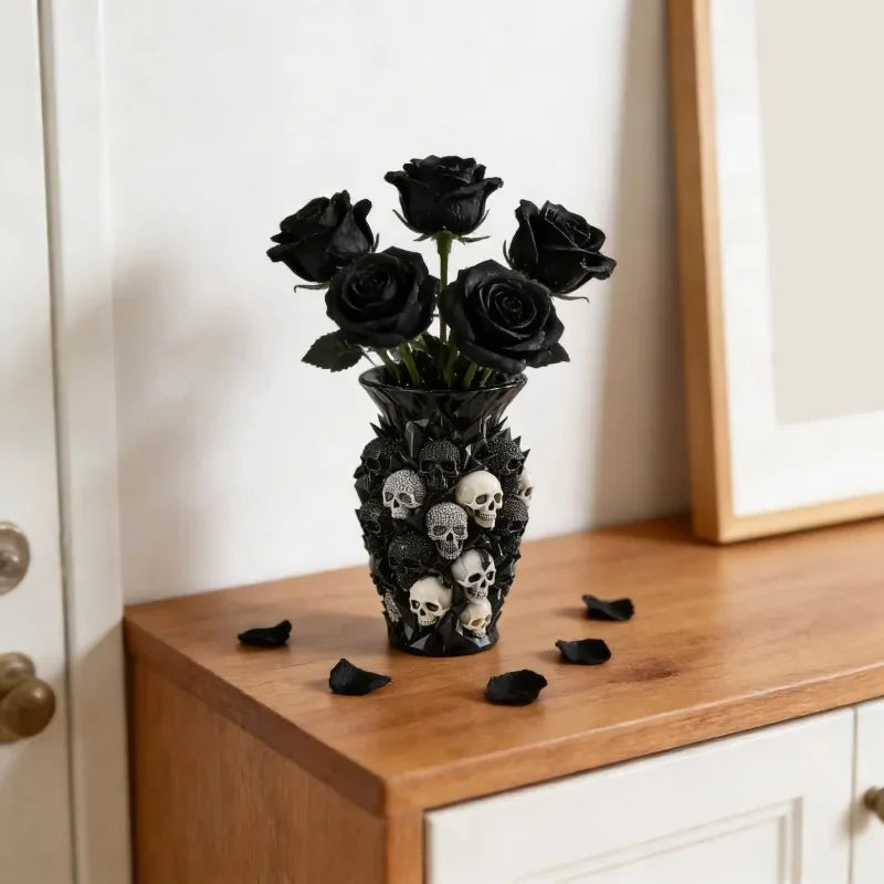 A black gothic skull resin decorative vase filled with dark roses and scattered skulls on a wooden surface.