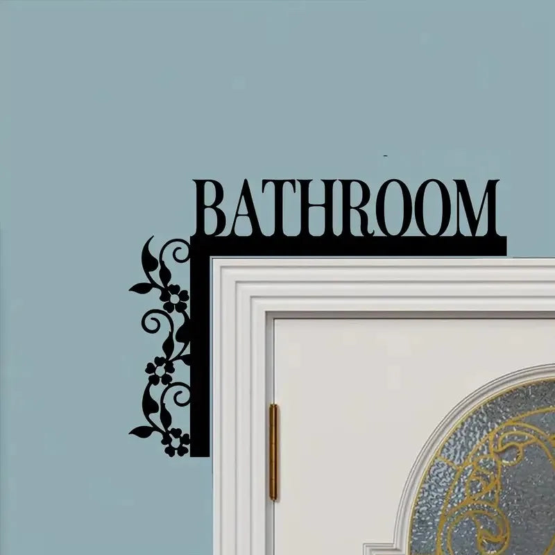 A black wrought iron floral design plaque is mounted above a white bathroom door frame on a light blue wall.