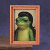 A cute green frog figurine displayed inside a wooden photo frame.
