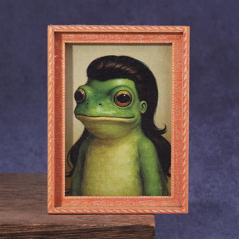 A cute green frog figurine displayed inside a wooden photo frame.