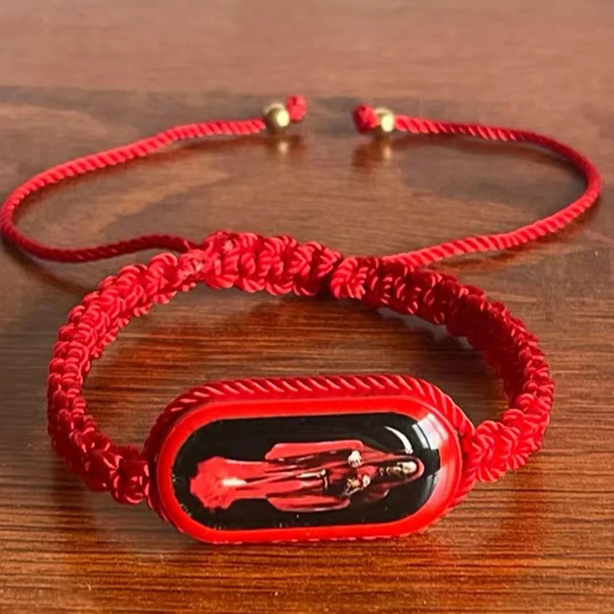 A red beaded bracelet with a rectangular red stone featuring a silhouette of the Virgin Mary.