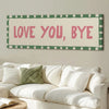 A framed canvas art print featuring the text LOVE YOU BYE in pink on a cream background with a green checkered border.