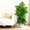 A vibrant green artificial papaya leaf plant in a white pot sits next to a white sofa.