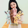 A woman holds several giant kawaii rabbit plush toys in various colors including blue, brown, pink, and yellow.