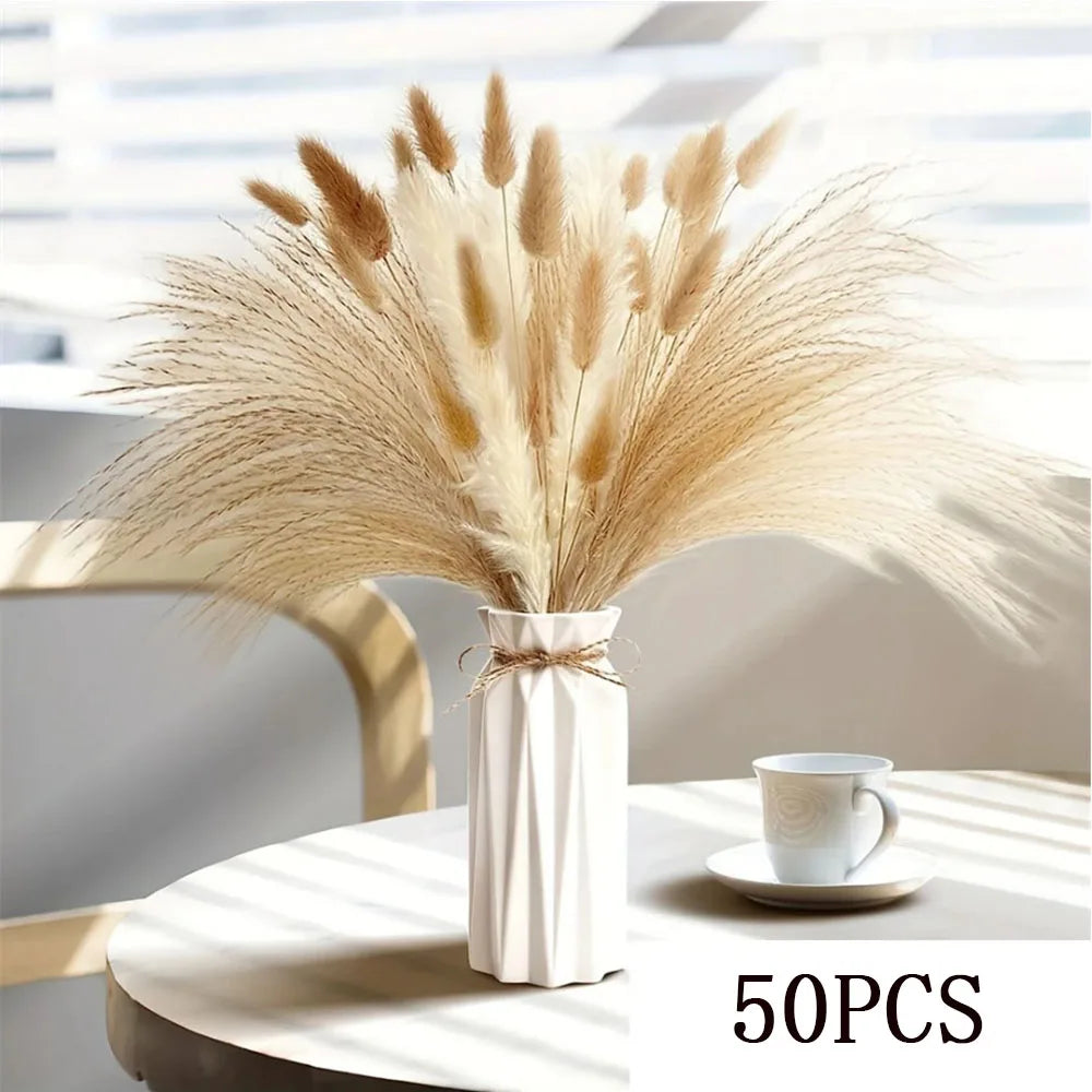 A bouquet of dried beige pampas grass flowers in a white vase on a light surface.