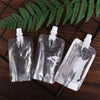 Three clear reusable squeezable liquid drink pouches resting on a dark wooden surface with a green fern leaf in the backgroun