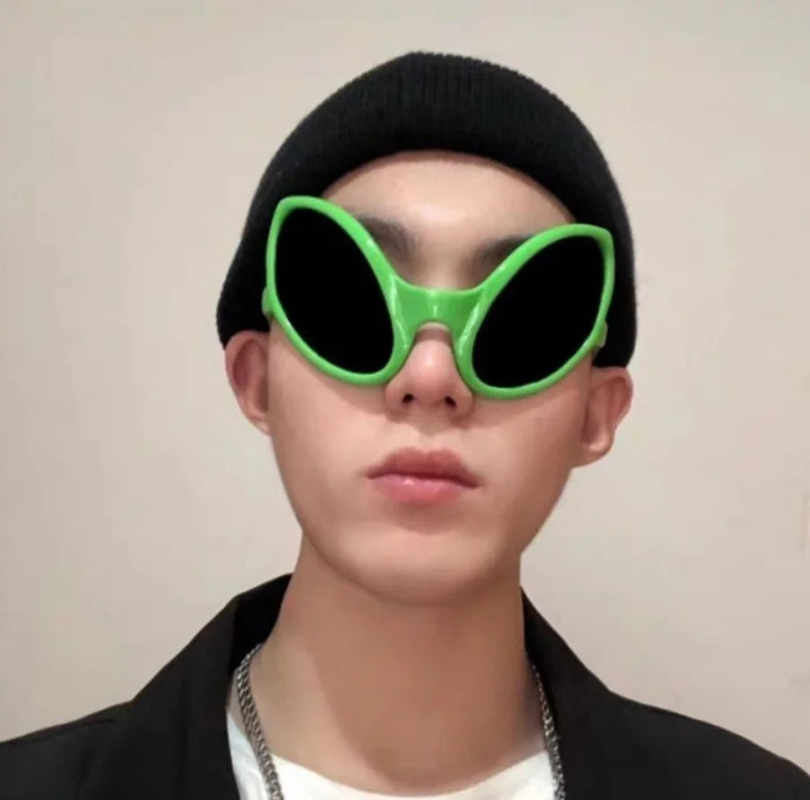 A close-up of a person wearing green alien sunglasses and a black beanie.