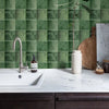 A kitchen countertop with a white sink and faucet set against a green tiled backsplash.