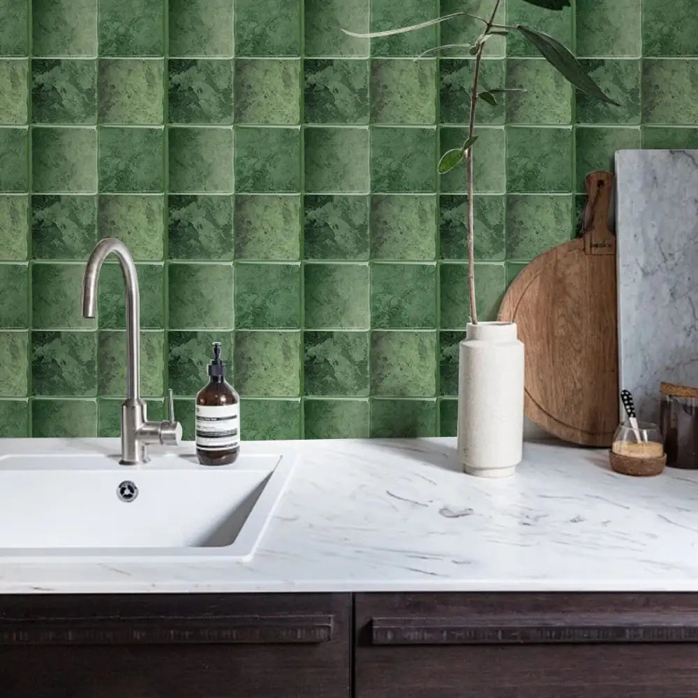 A kitchen countertop with a white sink and faucet set against a green tiled backsplash.