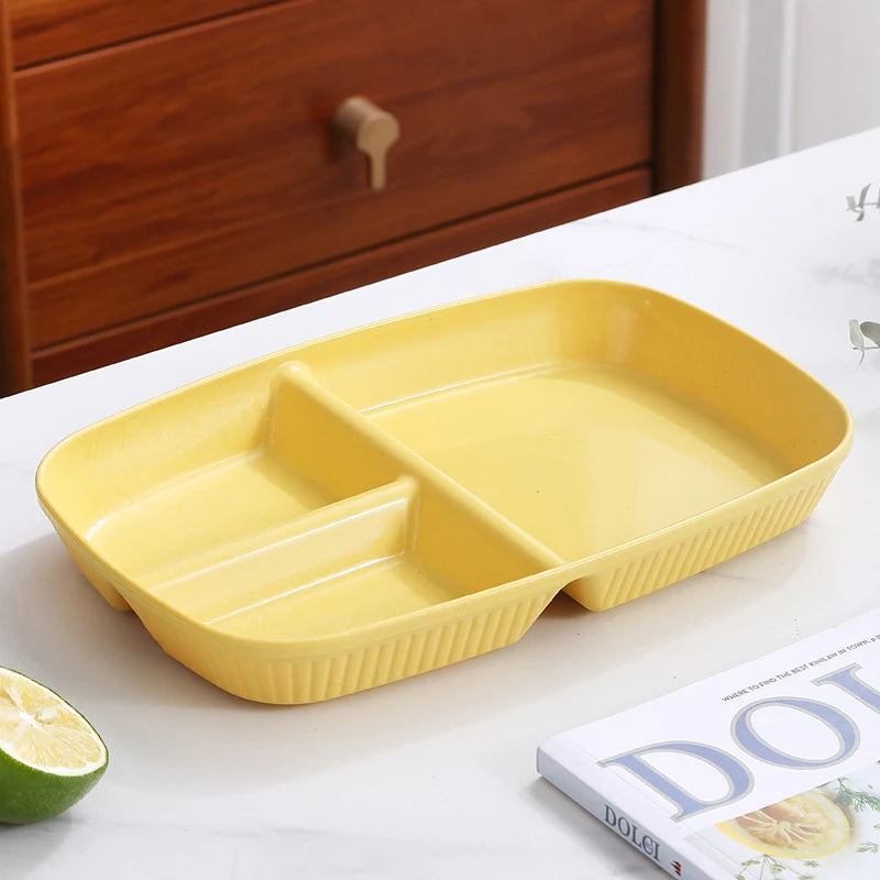 A yellow 3-compartment portion control plate is shown on a white surface next to a lime and a book.
