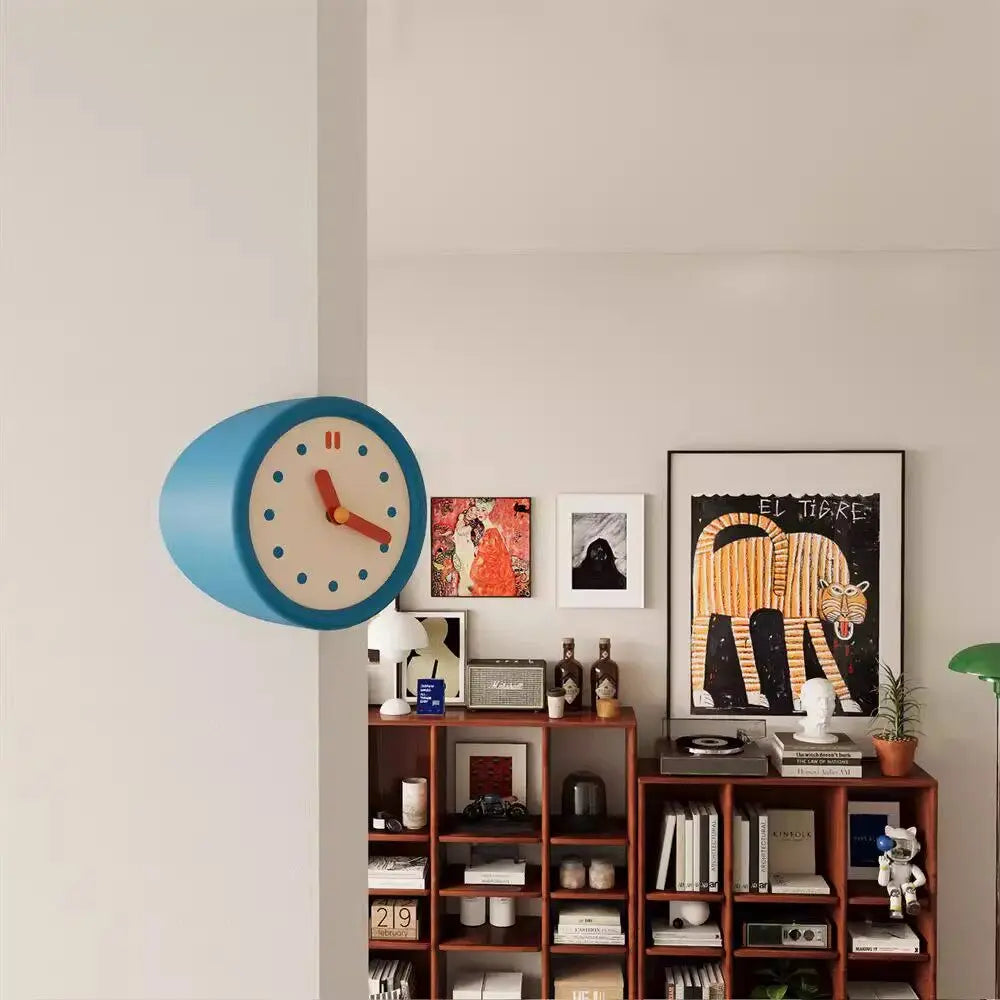 A blue modern resin wall clock is mounted on a white wall next to framed artwork.