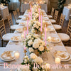 A long white table set for a wedding or banquet featuring gold accents and tall pink taper candles.