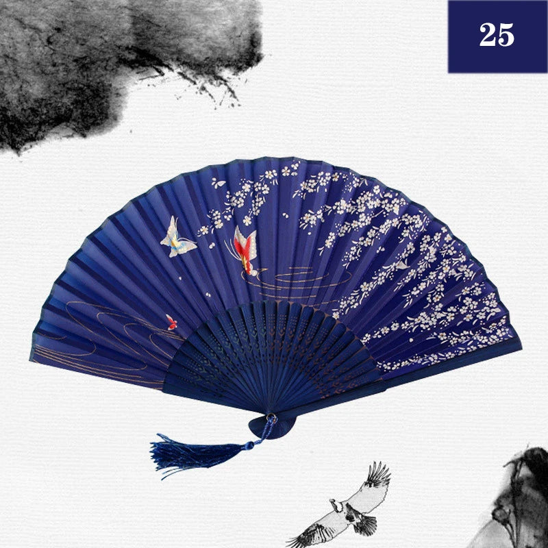 A dark blue vintage silk bamboo folding hand fan with white floral designs and a small bird detail.