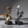 A set of three resin figurines depicting figures with large leaves or foliage, displayed on a dark surface.