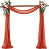 A wooden wedding arch decorated with orange chiffon draping fabric and floral arrangements.
