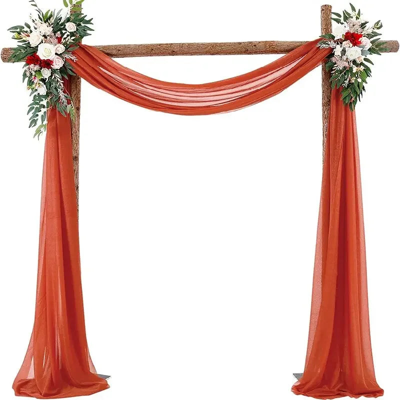 A wooden wedding arch decorated with orange chiffon draping fabric and floral arrangements.