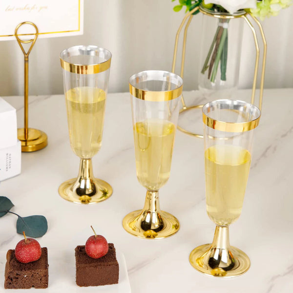 Four elegant gold-rimmed champagne flutes filled with pale yellow liquid are displayed on a white marble surface.