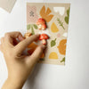 A hand is holding a set of nine colorful, cute decorative mushroom fridge magnets on a light pink background.