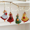 A set of four vintage wood angel ornaments with red and green accents hanging from a bare branch.