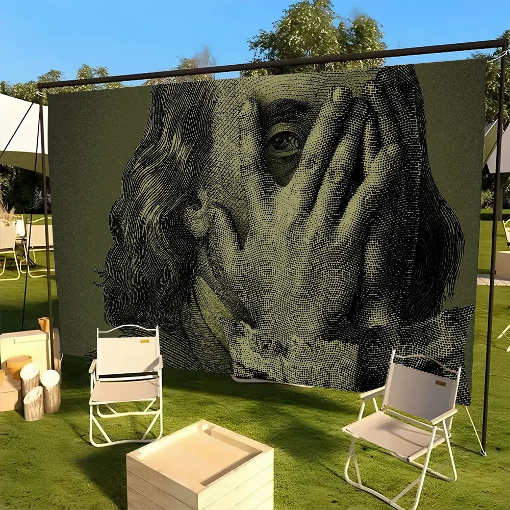 A large black and white print of a face covering its eyes with hands displayed outdoors on a green lawn.