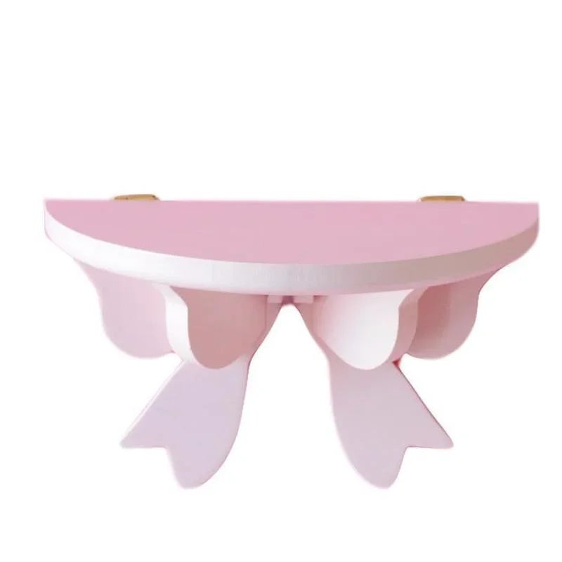 A pink decorative bow-shaped wooden wall shelf with a curved top and supportive legs.